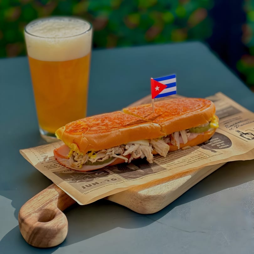 A Cubano's ATL Cuban sandwich with a Cuban flag pick and a glass of beer.