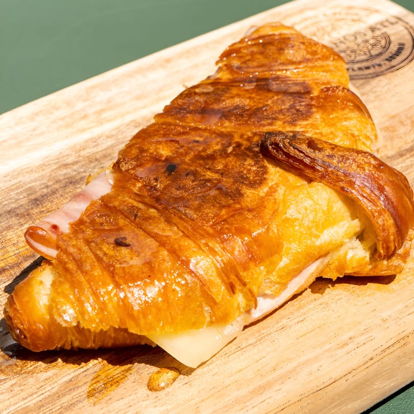 Golden-brown croissant filled with ham and melted cheese, served on a wooden board.